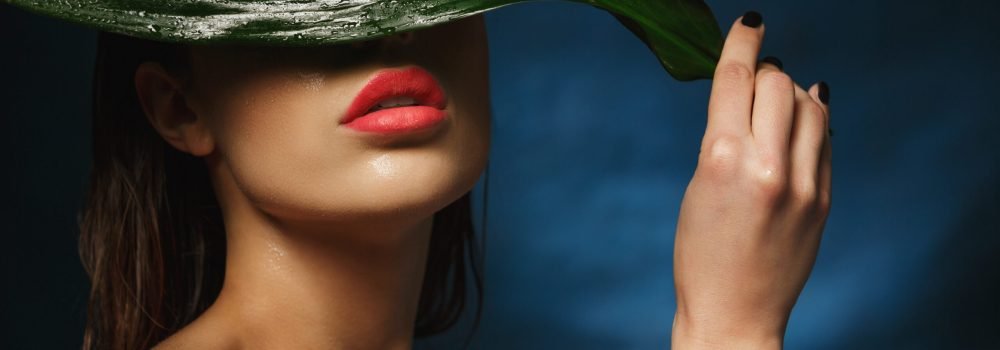 closeup of fit naked woman hiding under big wet leaf.